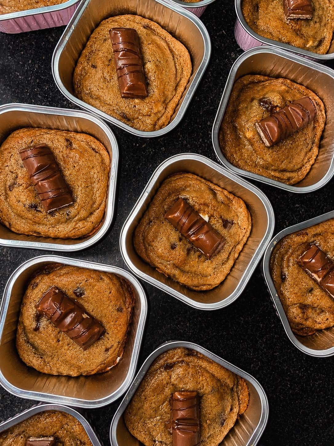 Kinder Bueno scoopies seen from above: soft baked chocolate chip cookies in square foil trays, each topped with a piece of Kinder Bueno.